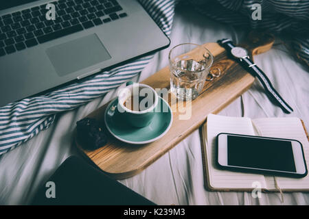Belle matinée à travailler au lit essentials : ordinateur portable et un nouveau café le matin avec de belles d'épaisseur sur un en bois crème fait-main rustique le bac Banque D'Images