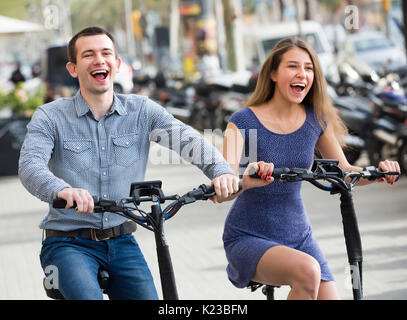 Jeune couple joyeux équitation sur les vélos électriques dans la ville rue . L'accent sur l'homme Banque D'Images