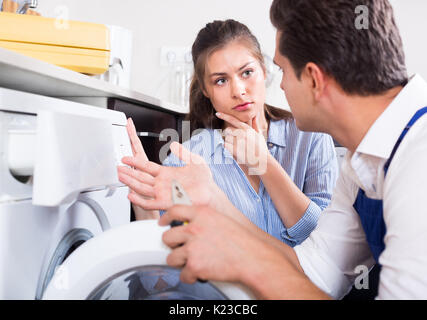 Jeune femme inquiète et mécanicien professionnel réparation lave-linge à la maison cuisine Banque D'Images