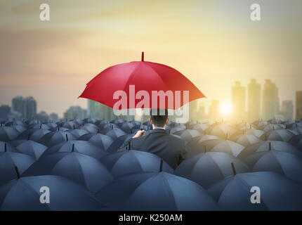 Parapluie rouge unique parmi les parapluies noir avec arrière-plan de la ville Banque D'Images