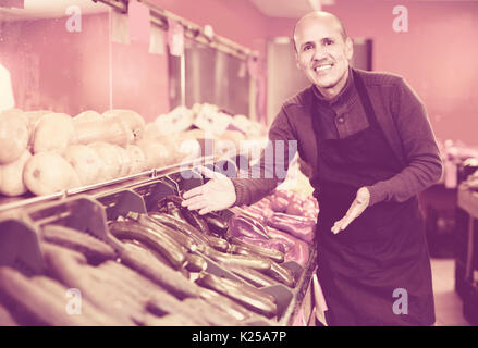 Portrait de friendly smiling young man in apron vente de légumes de saison au marché intérieur Banque D'Images