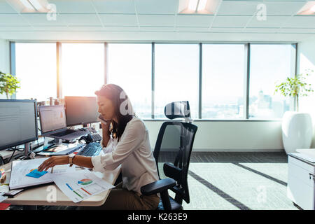 Femme entrepreneure regardant des papiers d'affaires tout en parlant sur téléphone portable. femme d'affaires assise à son bureau avec des ordinateurs et du papier de présentation Banque D'Images