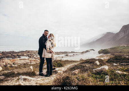 Jeune homme et femme debout ensemble à la plage en hiver d'usure. Couple au bord de la mer au cours de vacances d'hiver. Banque D'Images