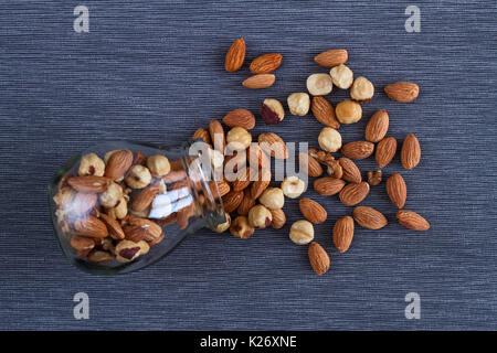 Les écrous appétissant de noix, amandes et noisettes dans un beau verre vase et sur un fond textile gris pour un petit déjeuner sain. Banque D'Images