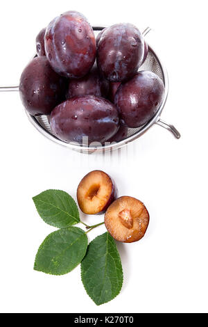 Avec passoire en acier prunes juteux doux, ensemble et la moitié des prunes mûres avec la feuille en face de la passoire isolé sur un fond blanc. Banque D'Images