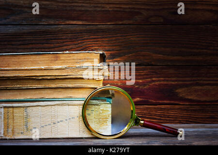 Une pile de vieux livres et la loupe sur fond de bois. Le concept de la recherche, l'étude de l'espace pour le texte. Banque D'Images