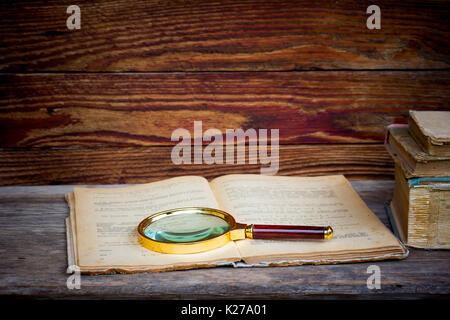 Vieux livre ouvert avec une loupe et une pile de livres sur une table en bois. Le concept de l'étude, l'étude de l'espace pour le texte. Banque D'Images