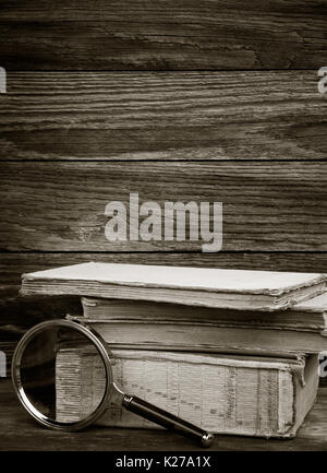 Photo en noir et blanc. une pile de vieux livres et la loupe sur fond de bois. Le concept de la recherche, l'étude de l'espace pour le texte. Banque D'Images