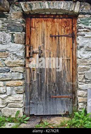 Vieille porte en bois dans la zone mur de pierre avec de grandes charnières rouillées et cadenas Banque D'Images