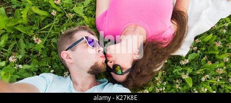 L'été, l'amour et personnes concept - happy woman in sunglasses lying on grass et prenant sur smartphone selfies Banque D'Images