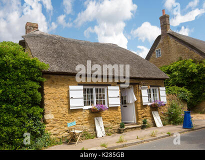 Maison en pierre avec toit de chaume et des volets aux fenêtres, utilisé comme magasin d'antiquités, au village historique d'Abbotsbury, Dorset, Angleterre sous le ciel bleu Banque D'Images