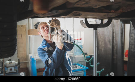 Homme caucasian worker - tournevis mécanicien de garage automobile réparation en atelier sous voiture levée Banque D'Images