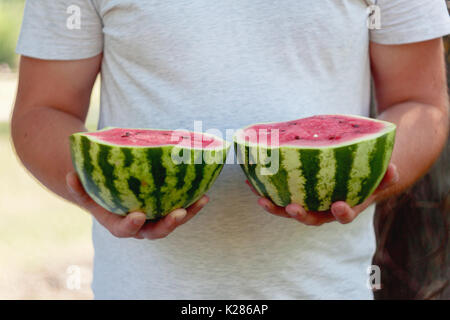 Un jeune homme est titulaire de deux moitiés de melon d'eau dans ses mains. Le concept d'une alimentation saine et le végétarisme. Banque D'Images