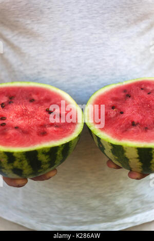 Un jeune homme est titulaire de deux moitiés de melon d'eau dans ses mains. Le concept d'une alimentation saine et le végétarisme. Banque D'Images