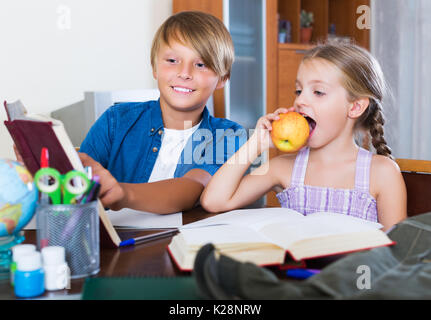 Portrait d'enfants positifs avec les manuels et notes in livingroom Banque D'Images