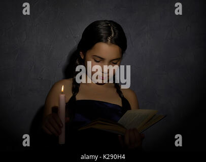 Little girl reading book et les études dans la lumière des bougies dans la pièce sombre Banque D'Images