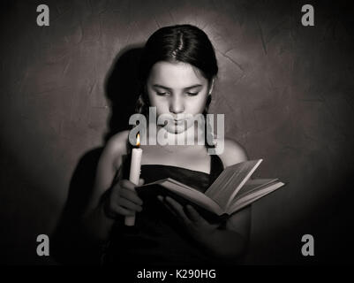 Little girl reading book et les études dans la lumière des bougies dans la pièce sombre Banque D'Images