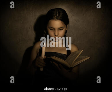 Little girl reading book et les études dans la lumière des bougies dans la pièce sombre Banque D'Images