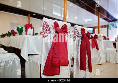 Chaises de mariage avec red bows attachés sur eux dans un restaurant. Banque D'Images