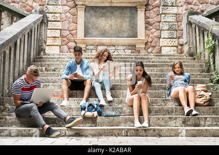 Étudiants adolescents avec des gadgets à l'extérieur sur les marches de pierre. Banque D'Images