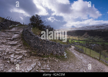 Sous ciel bleu, sentier ou piste de pierre, monte dans les courbes et en pierre sèche ronde, contre mur with Starbotton village, Wharfedale, Yorkshire, Angleterre, Royaume-Uni. Banque D'Images