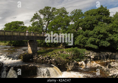 Jour d'été ensoleillé et les gens sont en bois passage passerelle sur Scenic Linton Falls Cascade - rivière Wharfe, Skipton, Yorkshire, Angleterre, Royaume-Uni. Banque D'Images