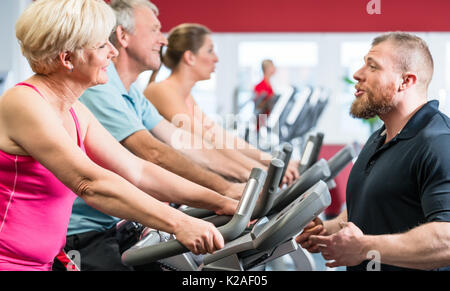 Entraîneur personnel indique à senior woman sur spinning au gy Banque D'Images