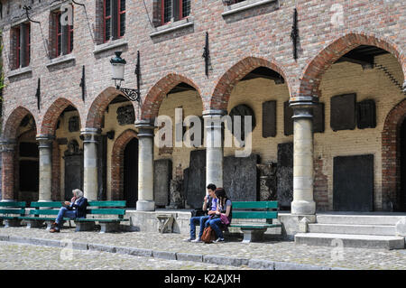 Trois personnes appréciant assis au soleil sur des bancs à l'extérieur de la cité médiévale de l'arches gruuthusemuseum dans la ville de Brugge / Bruges en Belgique Banque D'Images