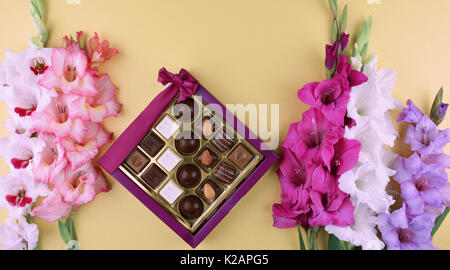 Belle glaïeul fleurs sur fond jaune avec de délicieux chocolats en boîte cadeau. Banque D'Images