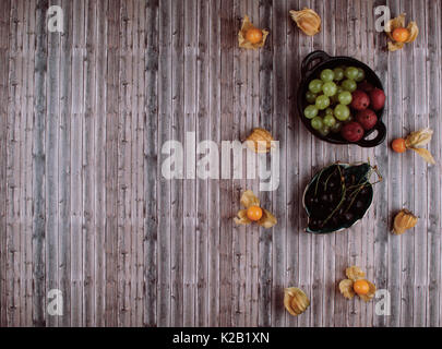 Groupe de juteux frais physalis bio, raisin vert et groseilles dans bol noir sur table en bois. Mise à plat de style. Banque D'Images