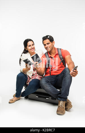 Stock photo de jeunes indiens couple packing for holiday, essayant de fermer valise pleine de vêtements, isolé sur fond blanc assis Banque D'Images