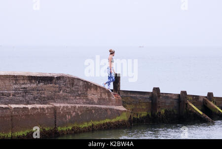 Jeune femme marchant le long de la paroi de la mer à Cromer, Norfolk portant des vêtements d'entraînement Banque D'Images