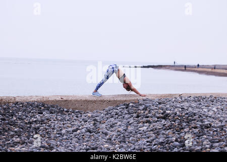 Young woman doing yoga on sea wall en Cromer, Norfolk, Royaume-Uni.
