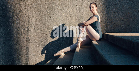 Ballerine assis à l'extérieur trouver une pose. Ballerine sitting on stairs s'étendant ses chevilles portant des pointes. Banque D'Images