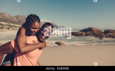 Jeune homme africain portant sa petite amie sur son dos à la plage. Couple aimant avoir piggyback fun sur mer. Banque D'Images
