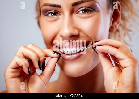 Close-up of a smiling girl with braces nettoyer les dents avec du fil dentaire. looking at camera. Banque D'Images