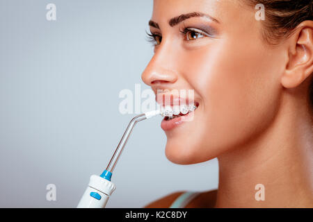 Souriante jeune femme à bretelles nettoyer ses dents à l'irrigateur oral. Banque D'Images