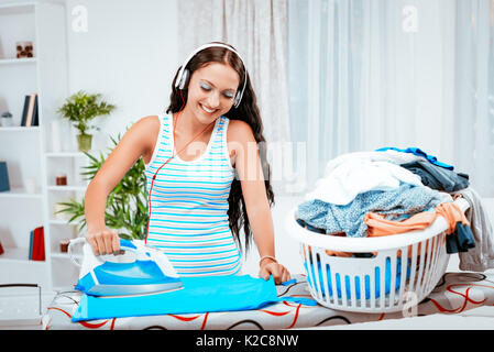 Young beautiful smiling woman ironing clothes et écouter la musique sur un casque. Banque D'Images