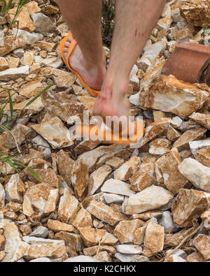 Un homme qui marche en chaussures inadéquates de tongs en plastique sandales ouvertes sur le sol accidenté de pierres et rochers Banque D'Images