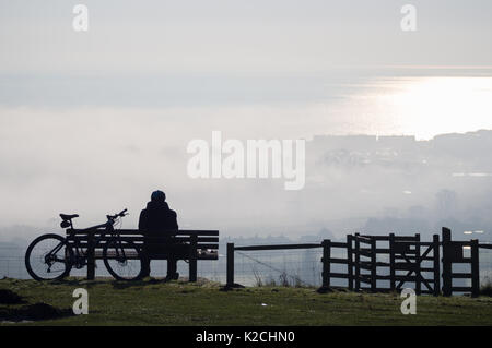 une personne solitaire assis banc de vélo de stationnement se pencher dans silhouette vue mer océan brouillard brumeux brouillard brumeux roulant Sandown sur terre Banque D'Images