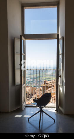 Une chaise pivotante moderne vide par une fenêtre ouverte sur un balcon avec portes vue de ciel bleu clair au-dessus de l'horizon des toits Banque D'Images