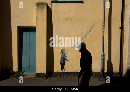 Vieil homme marchant dans la rue en whitstable kent, le vieil homme contraste très bien avec les graffitis de la Young boy blowing bubbles. Banque D'Images