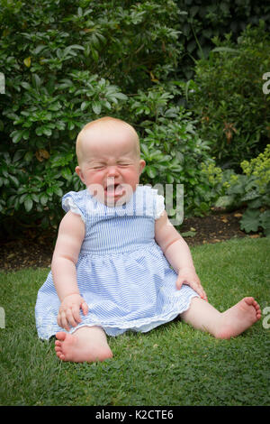 petite fille de 10 mois qui pleure avec colère tout en étant assise sur l'herbe. Banque D'Images