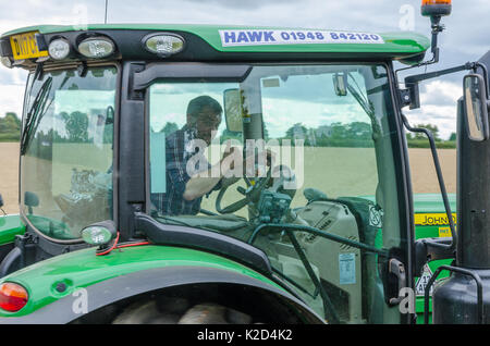 Le conducteur d'un tracteur John Deer donne un coup de pouce qu'il conduit passé Banque D'Images