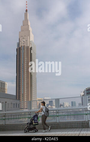 Une mère pousse une poussette en face de la Tour DoCoMo à Shinjuku, Tokyo, Japon Banque D'Images