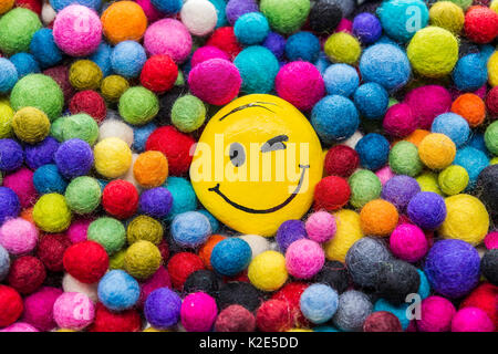 Smiley Face en pierre, peint en jaune, avec un clin d, se trouve entre boules de feutre coloré Banque D'Images