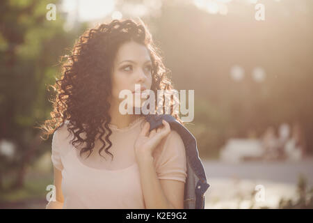 Une jeune fille avec des cheveux bouclés dans un parc de la ville. Portrait dans les rayons du soleil. Insouciante jeunesse Banque D'Images