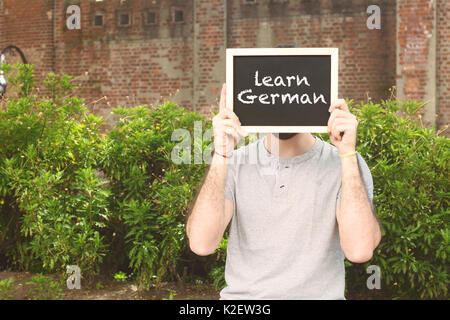 Portrait of handsome young man holding tableau sur lequel un texte 'Apprendre l'allemand". Concept de l'éducation. Banque D'Images