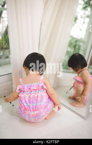 Peu cute asian baby girl jeu près de mirror à la maison Banque D'Images