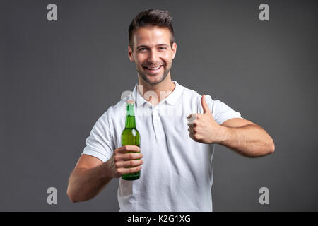 Un beau jeune homme se sentir heureux showing Thumbs up et tenant une bouteille de bière Banque D'Images